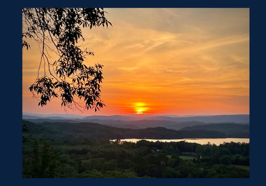 Sunset over Watts Bar Lake in Kingston Tennessee with rolling hills and tree branches in the foreground