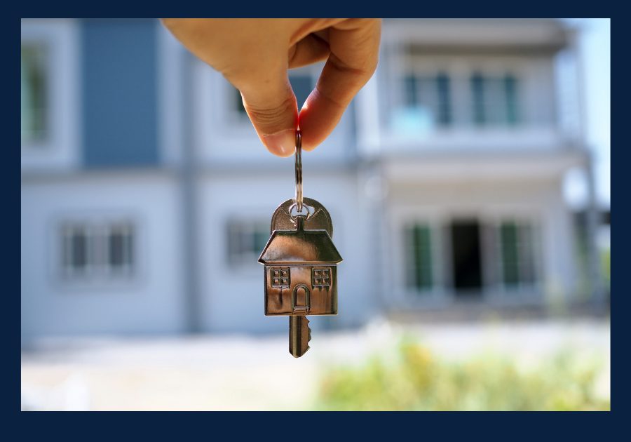 House key with a home-shaped keychain held in front of a new home