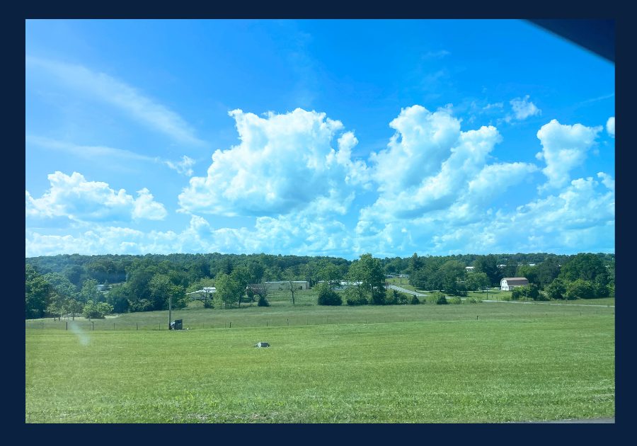 Open green fields and rural homes in East Tennessee under a blue summer sky.